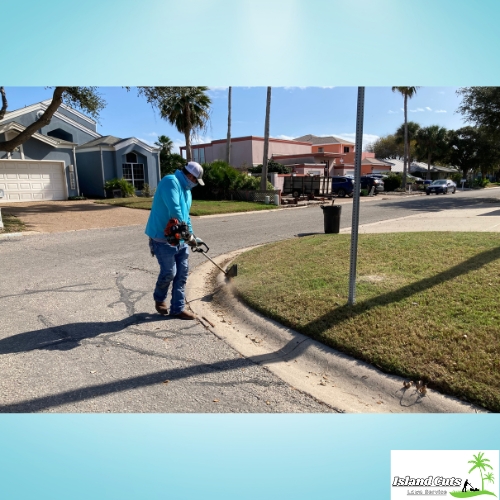 Worker from Island Cuts Lawn Service using an edger along a curbside on a sunny day.