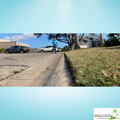 Lawn care professional from Island Cuts Lawn Service performing edging along a suburban street.